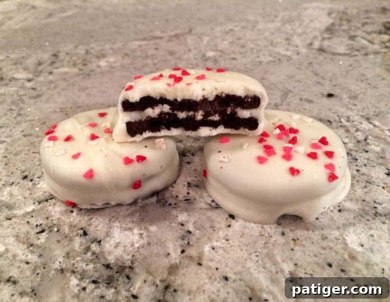 Love-Dipped White Chocolate Oreos 2 White Chocolate Covered Valentine's Day Oreos with heart sprinkles. One cookie is bit in half to show oreo inside.