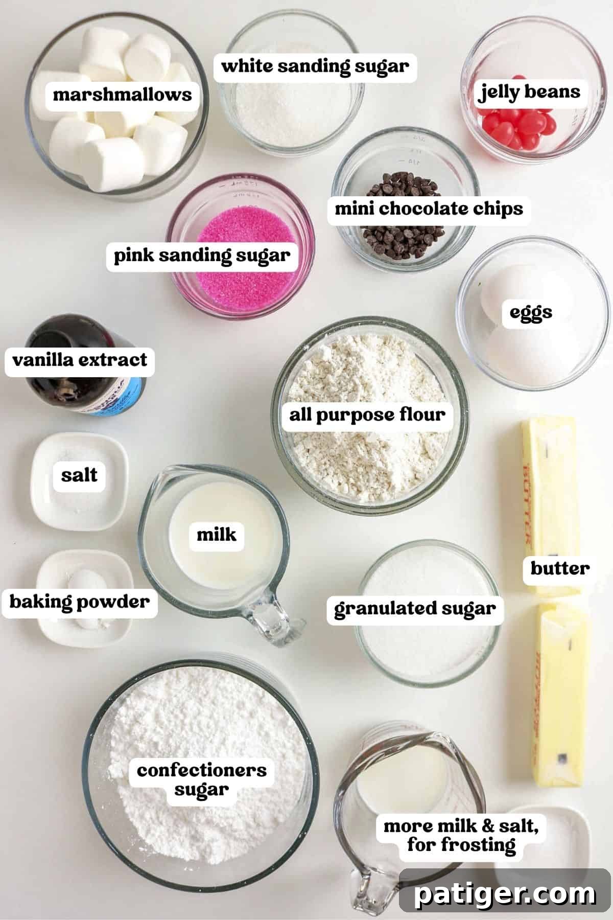 Fluffy Marshmallow Bunny Cupcakes 4 A flat lay photograph showcasing all the ingredients required for making Easter bunny cupcakes. Items are neatly arranged in bowls and include marshmallows, white and pink sanding sugar, jelly beans, mini chocolate chips, eggs, vanilla extract, salt, baking powder, milk, all-purpose flour, granulated sugar, butter, and confectioners sugar.