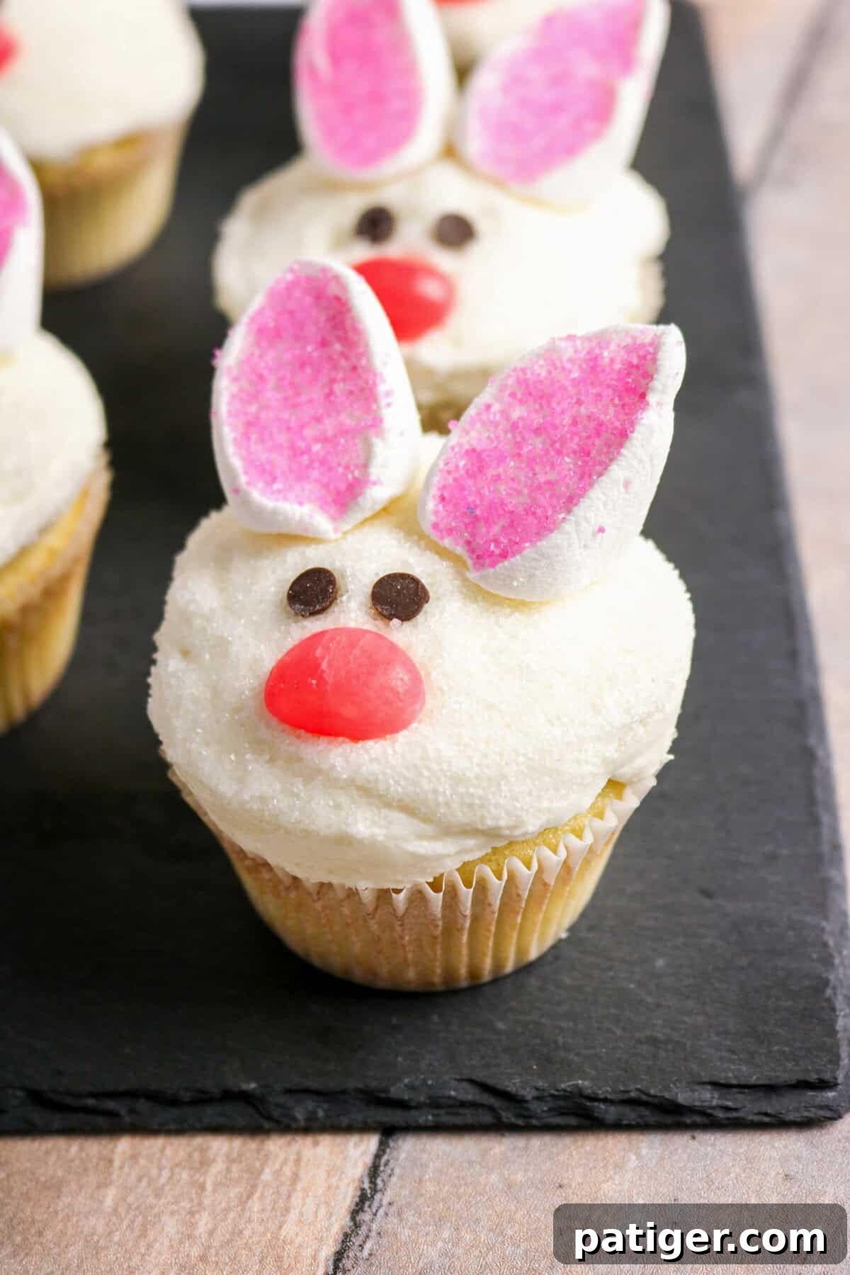 Fluffy Marshmallow Bunny Cupcakes 8 A collection of beautifully decorated bunny cupcakes with marshmallow ears and jelly bean noses, arranged on an elegant black slate serving board.