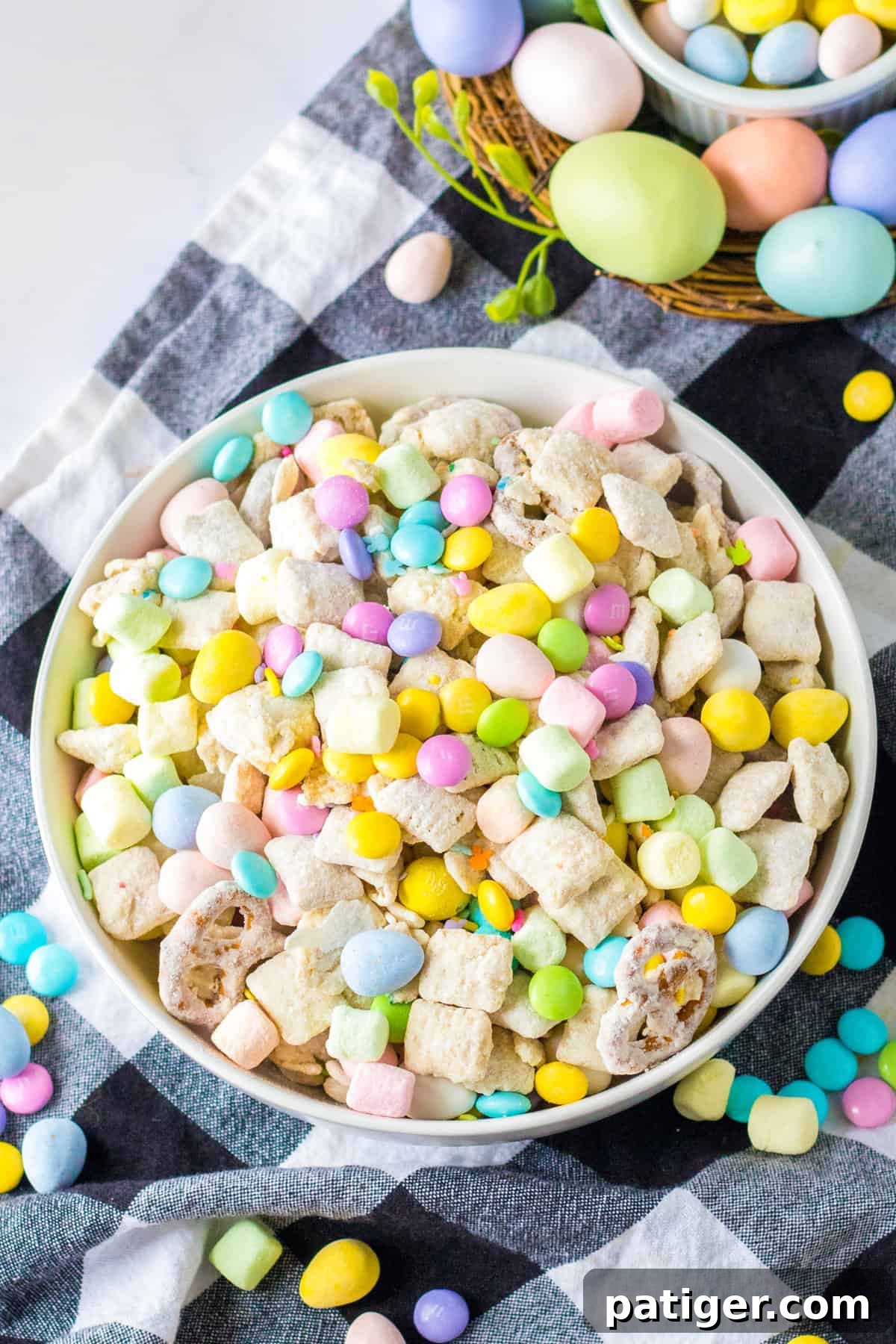 Easter snack mix in a large white serving bowl surrounded by Easter candies and egg decorations.
