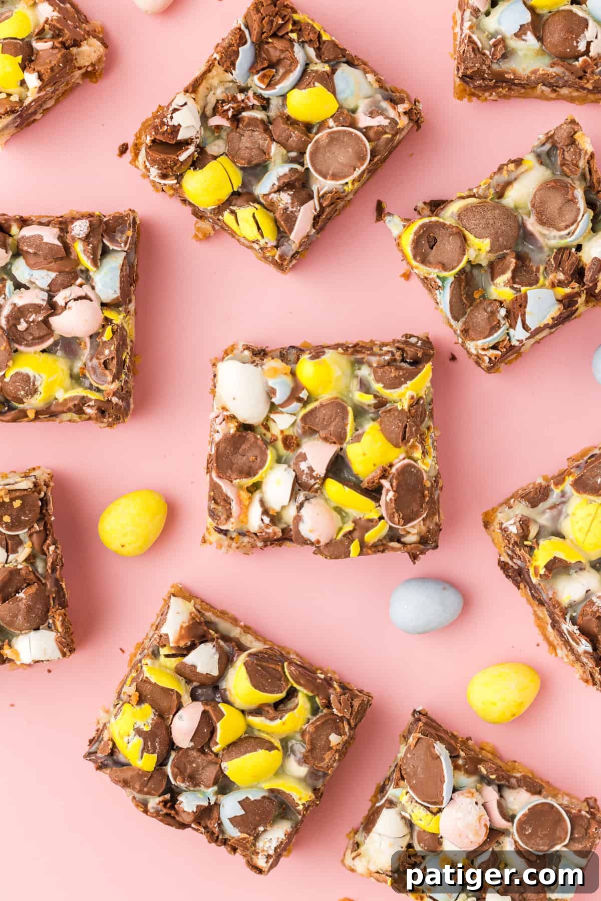 Easter magic cookie bars topped with crushed pastel mini eggs cut into squares and laid on a pink surface with additional mini eggs scattered around.