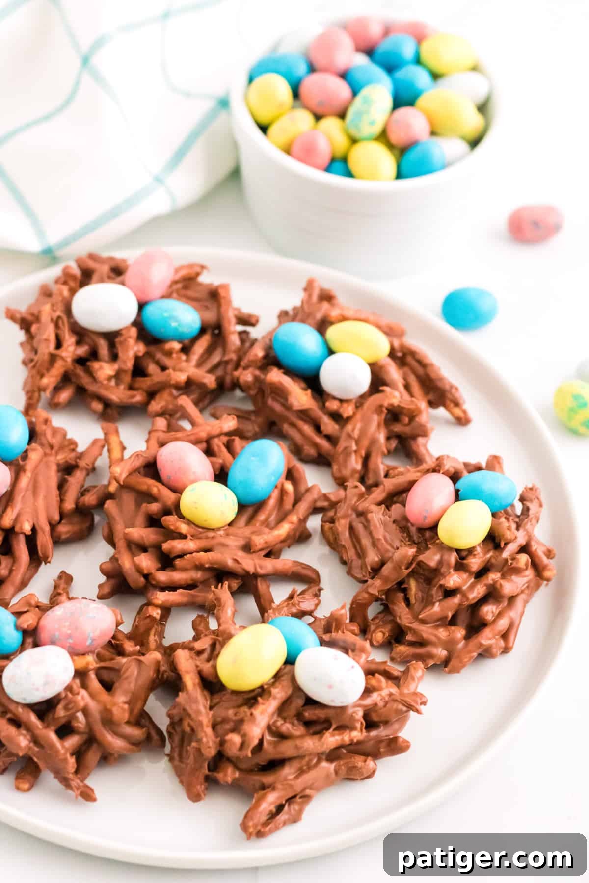 No-bake chocolate birds nest cookies arranged on a white plate with additional colored eggs in the background.