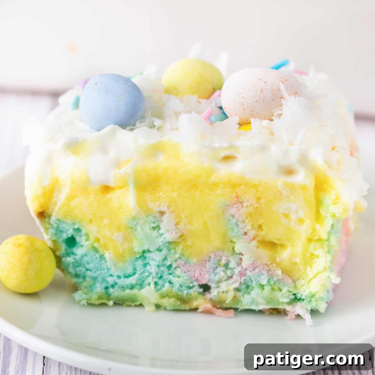 A slice of pastel Easter poke cake topped with whipped cream, coconut, and mini chocolate eggs.