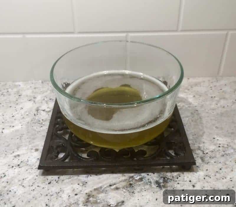 Completely melted shea butter and coconut oil mixture in a glass bowl, appearing clear, liquid, and ready for the next step of the body butter recipe.