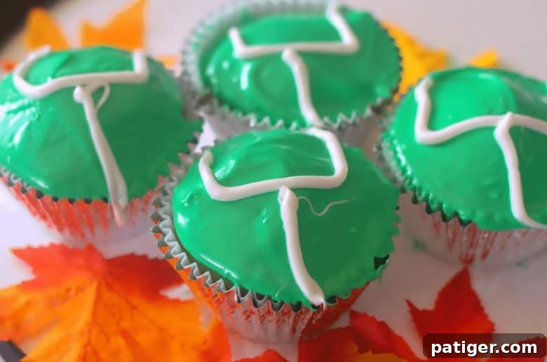 Vanilla cupcakes generously topped with bright green icing, featuring neatly piped white icing shaped as miniature football goalposts.