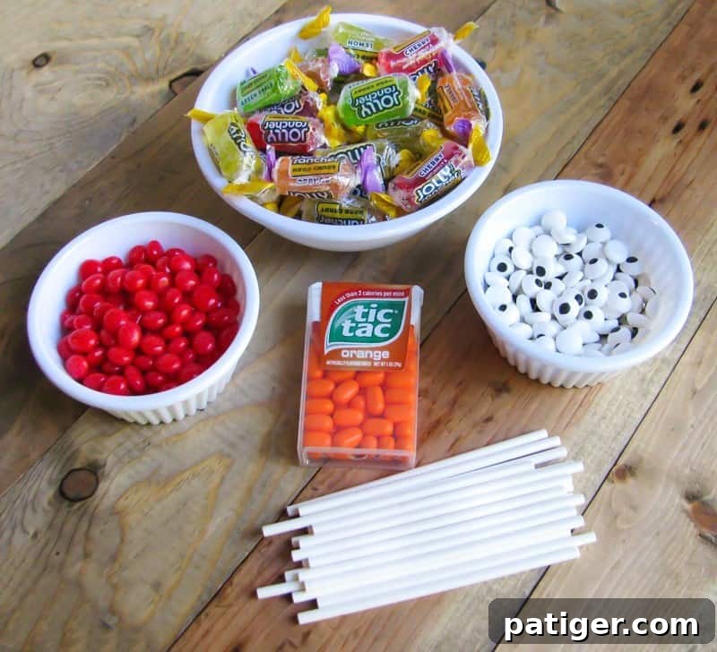 Bowl of Jolly Ranchers, bowl of red hots, bowl of candy eyeballs, container of orange tic tacs, and lollipop sticks.