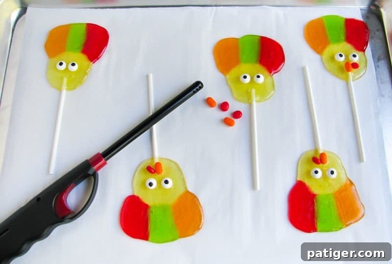 Handheld lighter, candies, and in process lollipops on lined baking sheet.