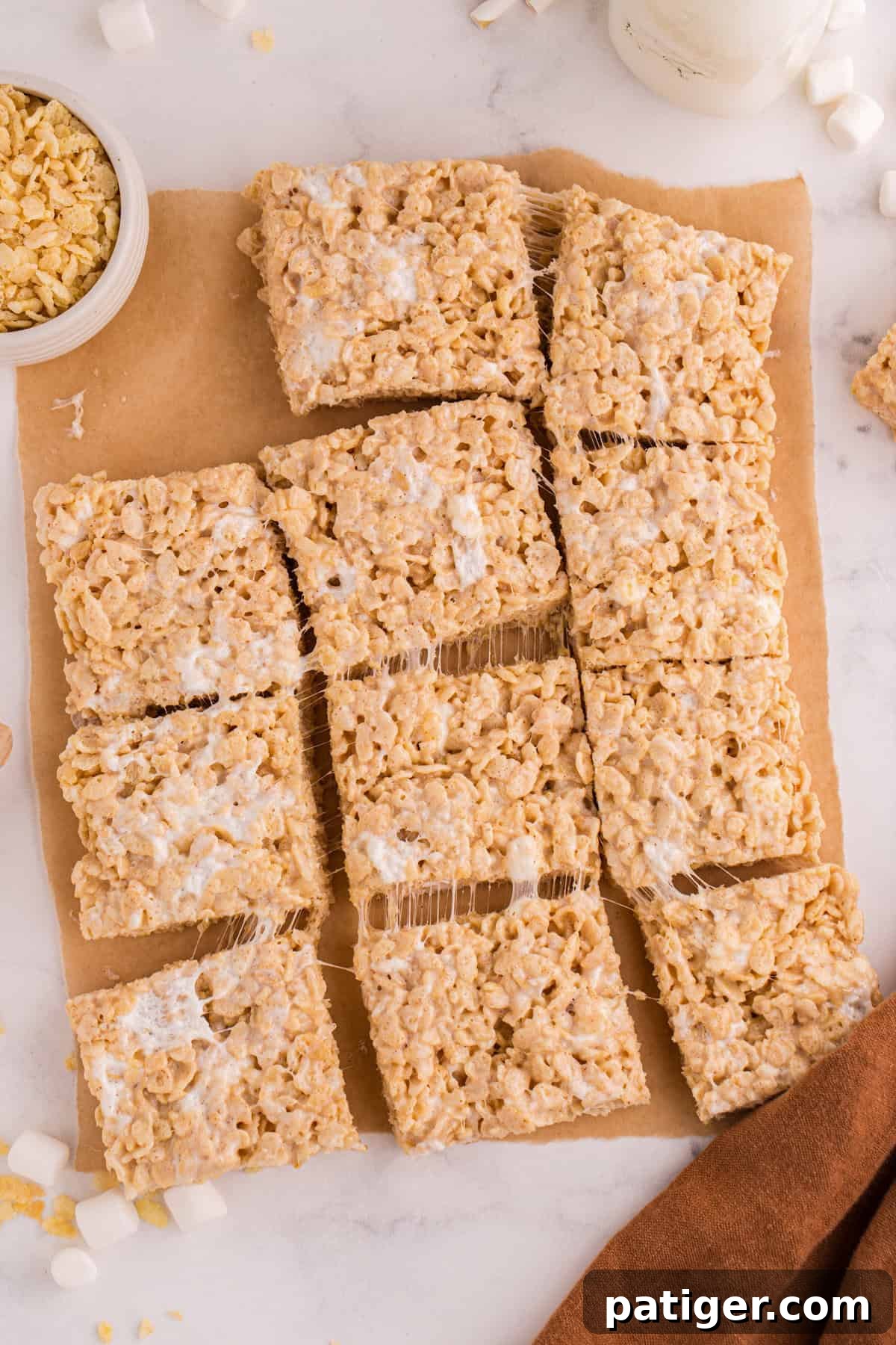 Top-down close-up of cut brown butter Rice Krispie treat squares on parchment paper, with melted marshmallows stretching between the pieces.