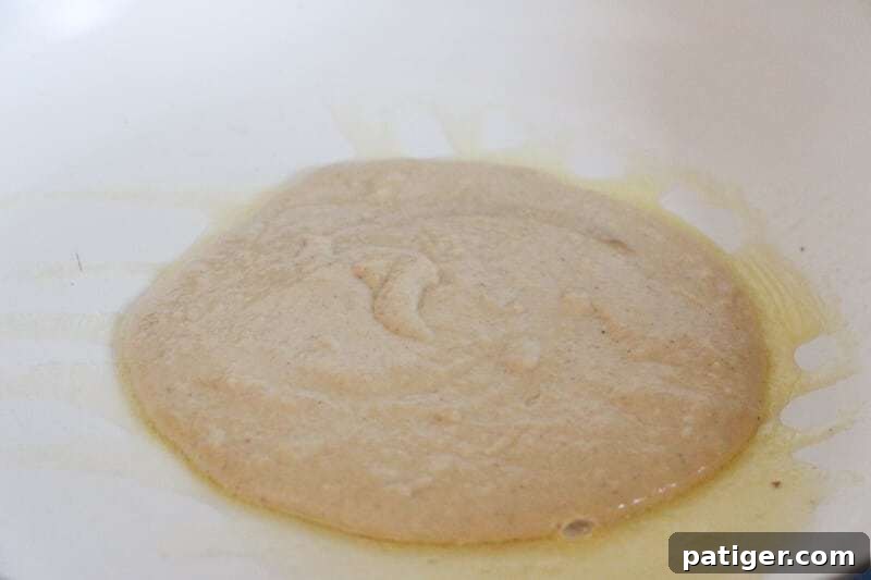 Pancake batter being poured into a hot frying pan, forming round gingerbread pancakes that will soon begin to bubble.
