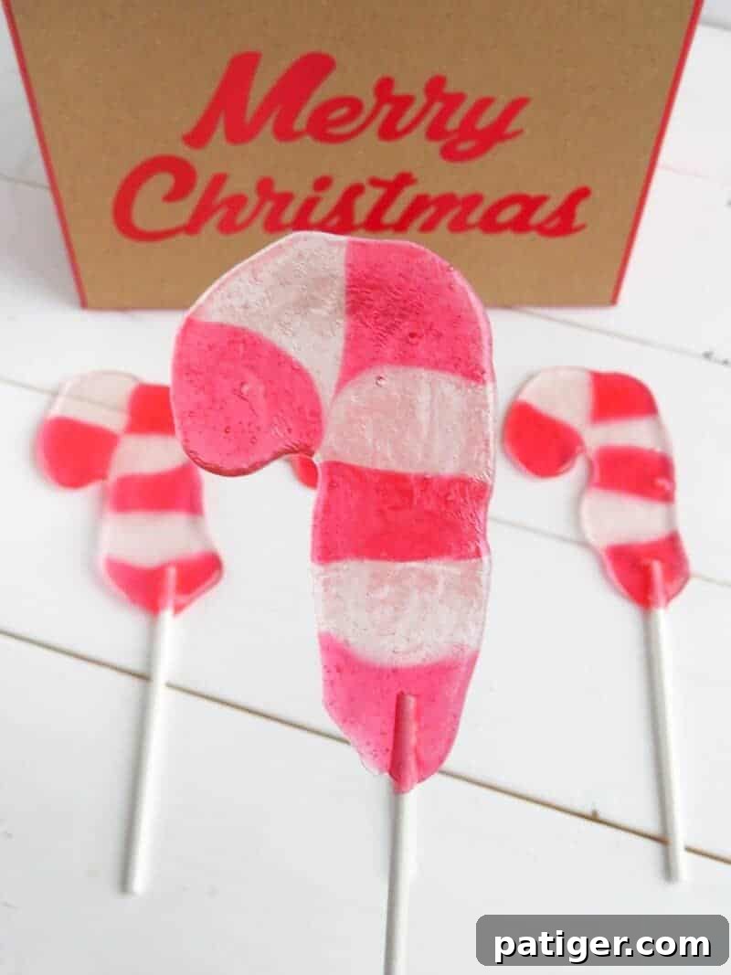 Close-up of a festive Candy Cane Lollipop on a white stick, with two more blurred in the background, showcasing its vibrant red and white stripes.