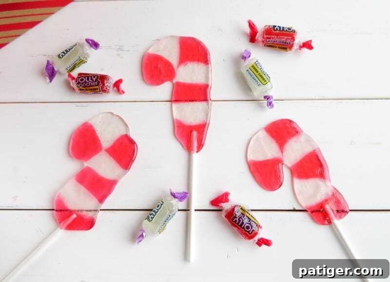 Candy cane shaped lollipops arranged on a rustic white wooden background, surrounded by scattered strawberry and pineapple Jolly Rancher candies.