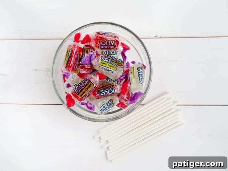 Bowl filled with unwrapped red and white Jolly Ranchers, with a stack of white lollipop sticks next to it, ready for crafting candy cane lollipops.