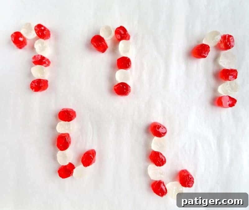 Cut red and white Jolly Ranchers precisely placed on a parchment-lined baking sheet, forming multiple candy cane shapes with alternating colors.