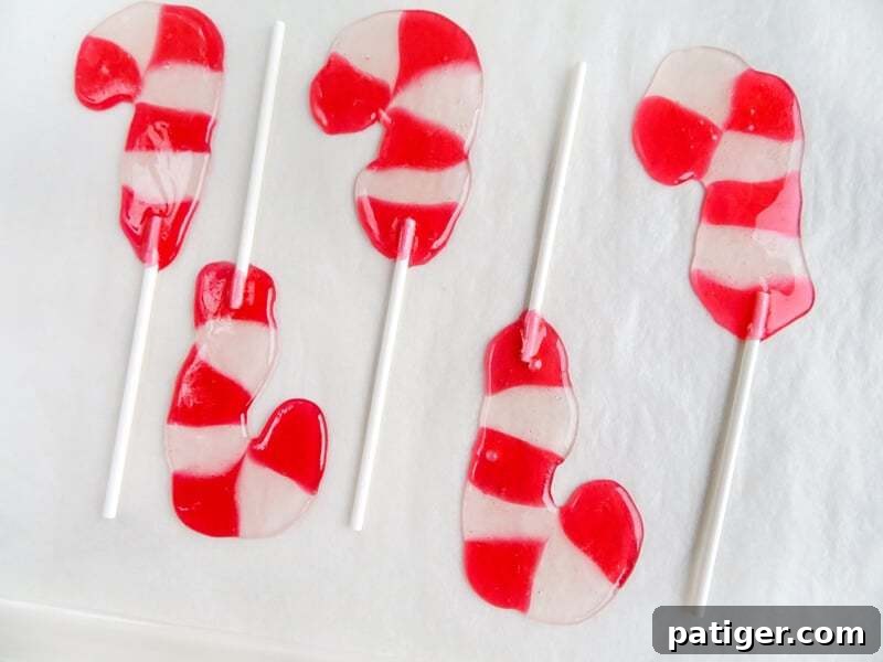 A baking sheet featuring freshly melted Jolly Ranchers molded into candy cane lollipops, with sticks inserted, showcasing the completed baking stage.