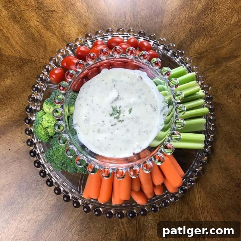 An inviting bowl of homemade bacon ranch dip, beautifully presented on a rustic wooden board and surrounded by a colorful and healthy assortment of fresh vegetables like carrot sticks, celery, and vibrant bell pepper strips, making for a healthy and appealing dipping platter.
