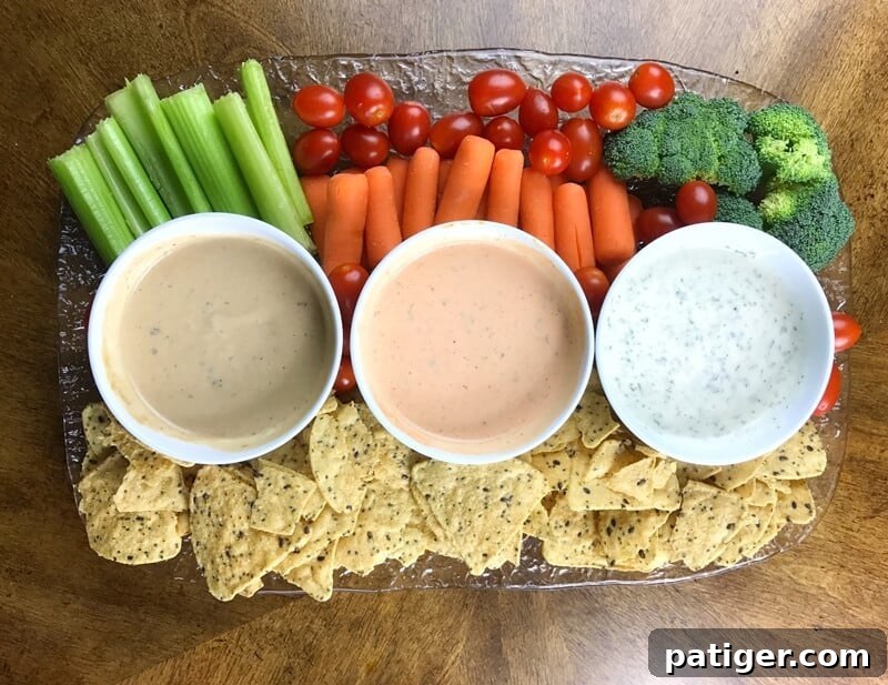 A beautifully arranged platter showcasing three distinct ranch-based dips, each perfectly paired with a colorful selection of fresh vegetables and golden tortilla chips, illustrating the incredible versatility of Litehouse Homestyle Ranch Dressing as a dip base.