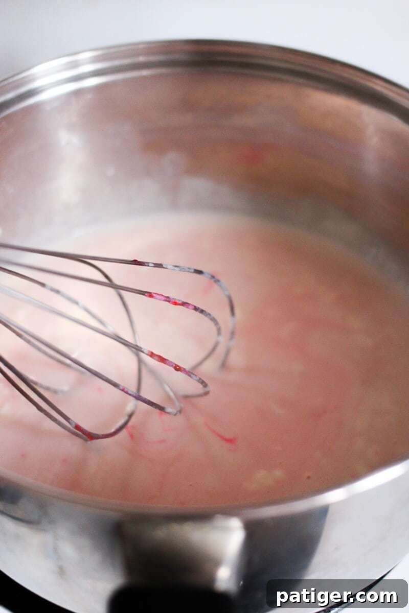 Whisk being used in a bowl of pink velvet hot chocolate mixture.