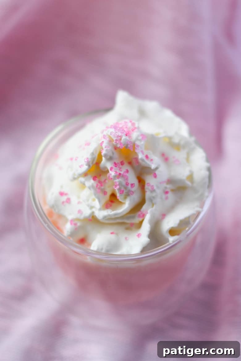 Pink hot chocolate in a glass mug with whipped cream and pink sanding sugar.