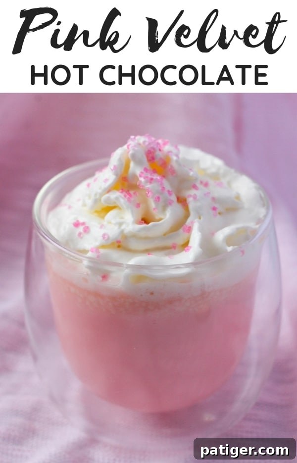 Pink Velvet Hot Chocolate served in a mug with whipped cream and sprinkles.