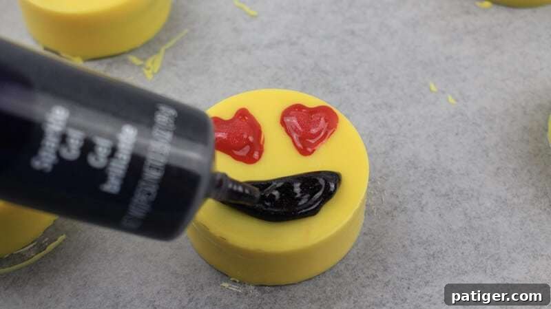Mouth being added with black gel to a heart eyes emoji Oreo.