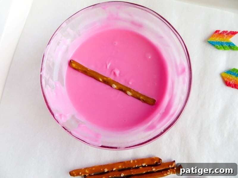 Pretzel sticks being dipped in melted pink candy.