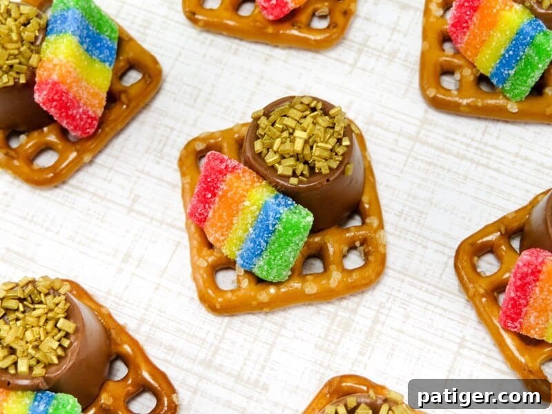 Close-up shot of a single St. Patrick's Day Pot of Gold Pretzel bite, showcasing the melted Rolo, gold sprinkles, and rainbow candy against a festive green background.