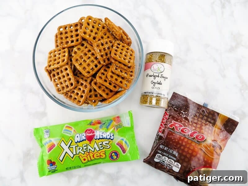 A flat lay image of the four ingredients for St. Patrick's Day Pot of Gold Pretzels: square pretzels, Rolo candies, Xtreme Airhead Rainbow Bites, and gold sugar crystals.
