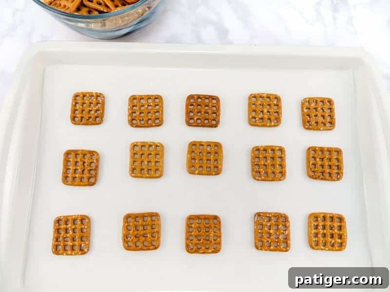 Fifteen square waffle-style pretzels are neatly arranged in three rows on a baking sheet lined with parchment paper, ready for the next step of the recipe.