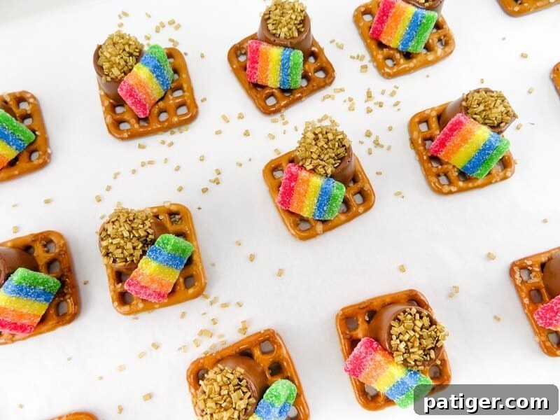 Finished St. Patrick's Day Pot of Gold Pretzels, each with a melted Rolo, gold sprinkles, and a rainbow candy, cooling on a baking sheet.