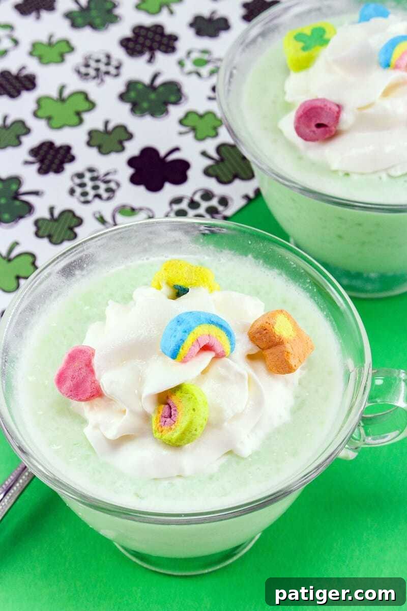 Shamrock Swirl Frozen Hot Chocolate 2 Vibrant green frozen hot chocolate in a mug, topped with fluffy whipped cream and colorful Lucky Charms marshmallows. Shamrocks are blurred in the background, hinting at St. Patrick's Day celebrations.
