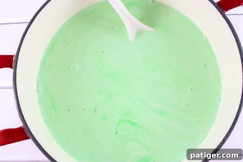 Shamrock Swirl Frozen Hot Chocolate 6 A pot on a stove containing a vibrant green, creamy liquid being stirred with a white spoon, indicating the preparation of the hot chocolate base.