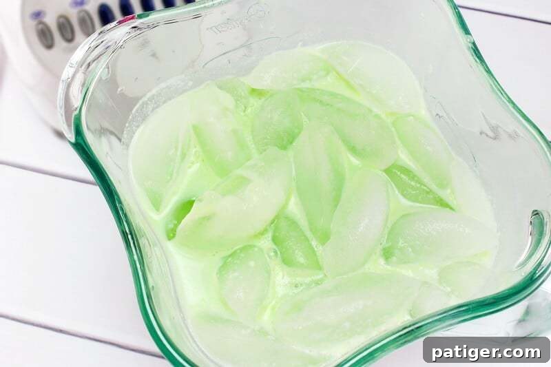 Shamrock Swirl Frozen Hot Chocolate 7 A blender jug filled with a vibrant green liquid and ice cubes, ready to be blended into a frozen drink.