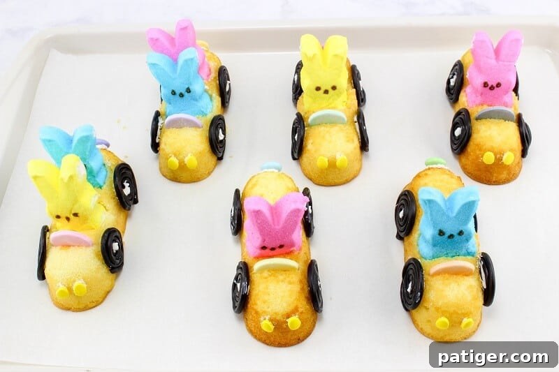 Six Peeps Twinkie cars on lined baking sheet setting after having their wheels stuck on with melted candy melts.