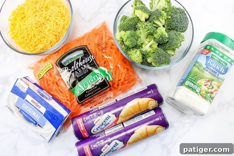 Collection of fresh ingredients for veggie pizza bars on a clean countertop: a package of crescent rolls, a block of cream cheese, a bowl of shredded cheddar cheese, a pile of shredded carrots, fresh broccoli florets, and a packet of ranch seasoning.
