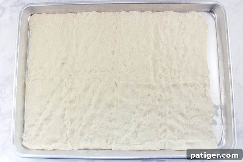Crescent roll dough evenly spread out on a baking sheet, ready for the oven to become a crispy base.