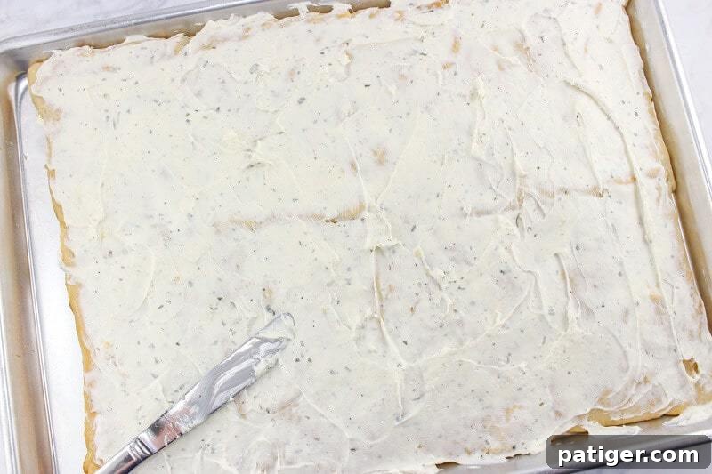 The savory cream cheese mixture spread smoothly over the cooled crescent roll base, creating an even layer.