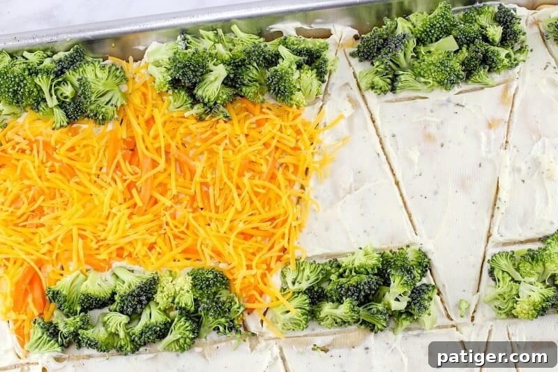 A close-up view of the veggie pizza bars on the baking sheet, topped with vibrant shredded carrots, cheddar cheese, and green broccoli florets, beautifully arranged into carrot shapes.