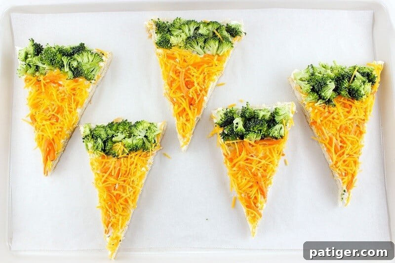 Individually cut slices of carrot and broccoli veggie pizza bars arranged on the baking sheet, showcasing their appealing shapes and colorful toppings.