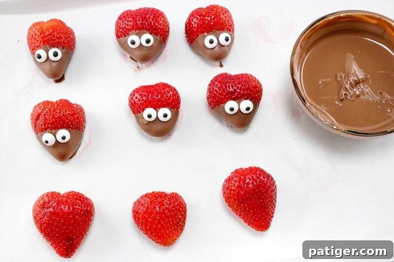 Strawberries with their bottom third dipped into melted chocolate and candy eyes pressed on top.