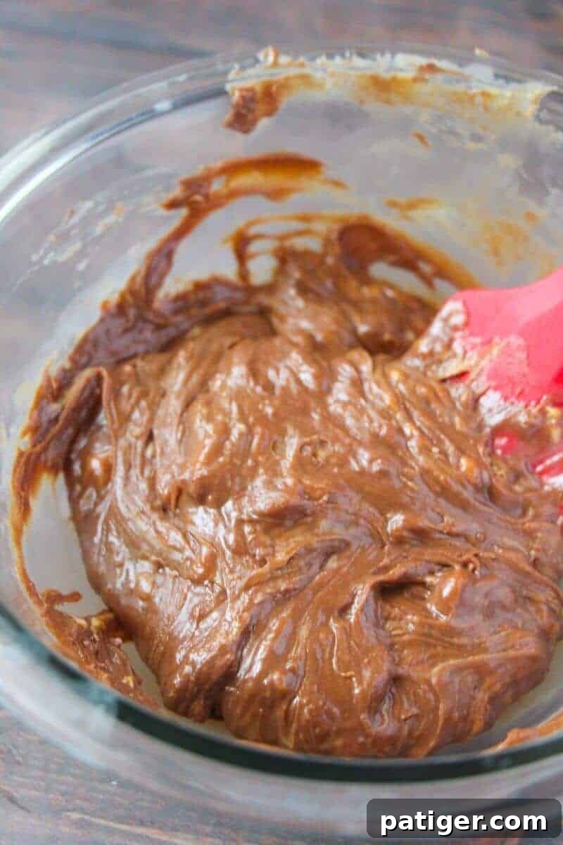 Melted ingredients being stirred together with a silicone spatula in glass bowl.