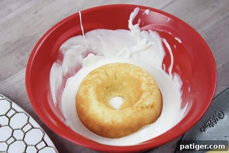 Baked cake donut being dipped in a bowl of melted white candy, creating the eyeball base.