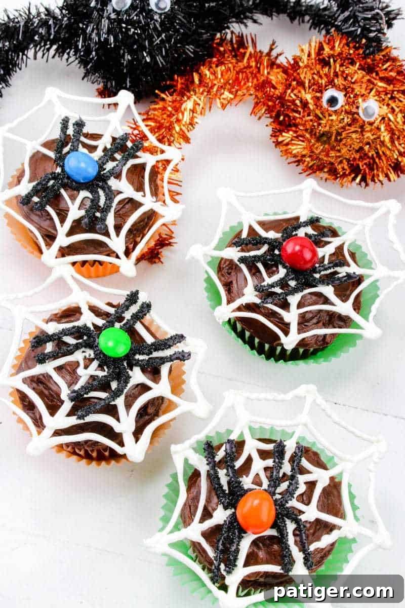 Four Halloween spider web cupcakes with blue, red, green, and orange M&Ms as the spider's bodies.