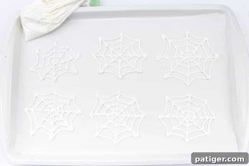 Six white candy spiderwebs on parchment lined baking sheet.