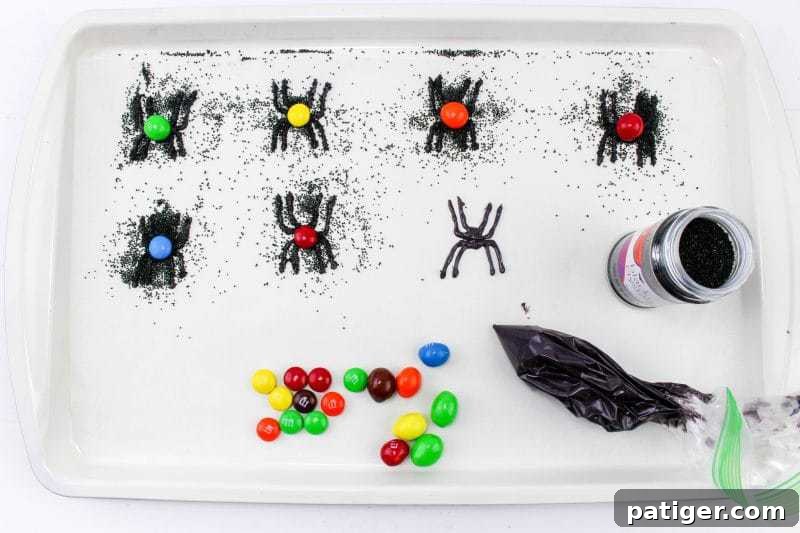 Candy spiders covered with black sanding sugar on a lined baking sheet. Some have colorful M&Ms on their backs.