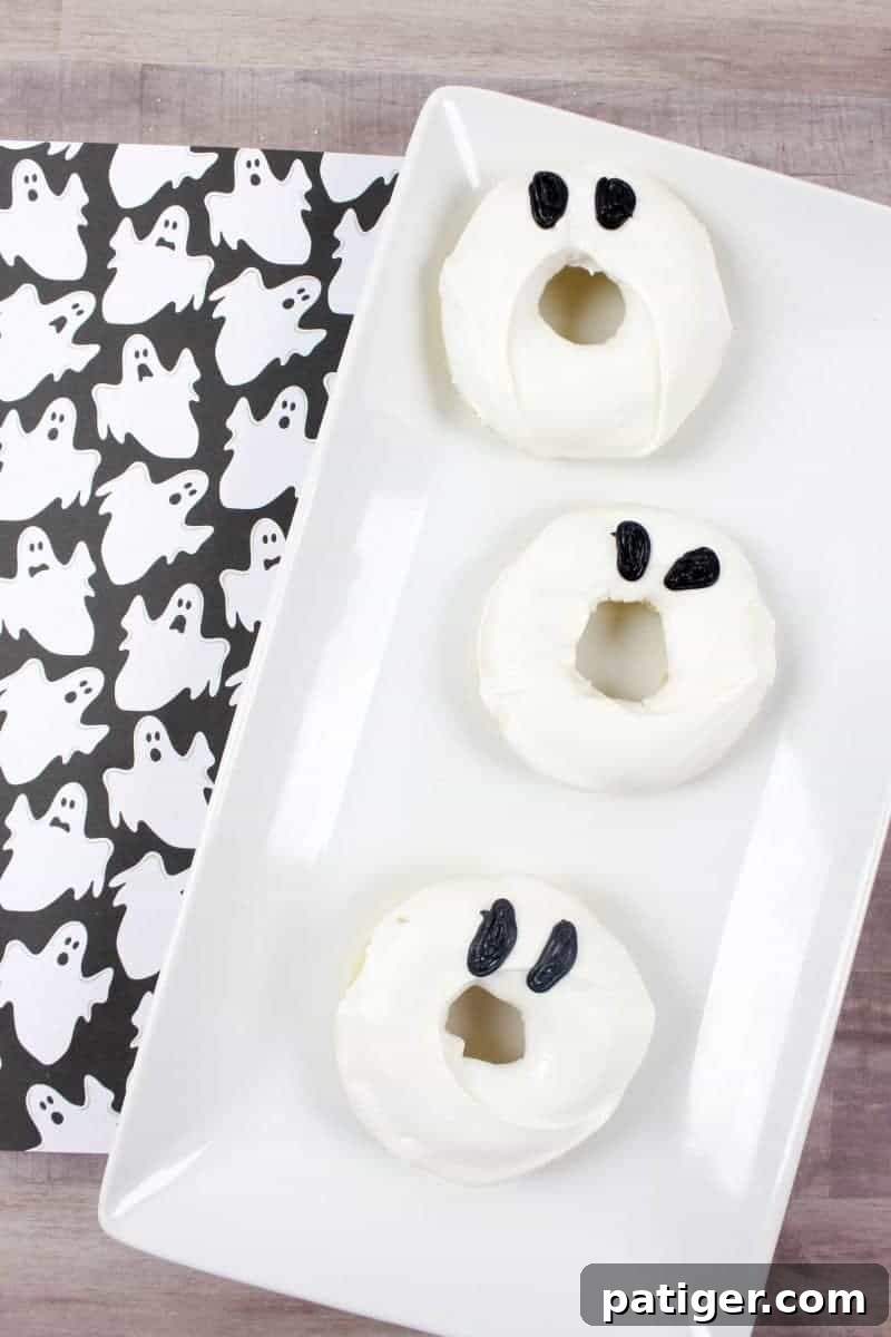 A plate of freshly baked ghost doughnuts with white candy melt frosting and black gel icing eyes. Quick and easy Halloween dessert recipe.