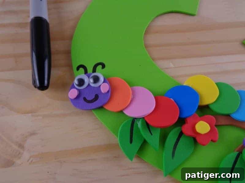 The completed caterpillar is carefully glued onto the branch of the letter C, and antennae are drawn on the letter behind its head.