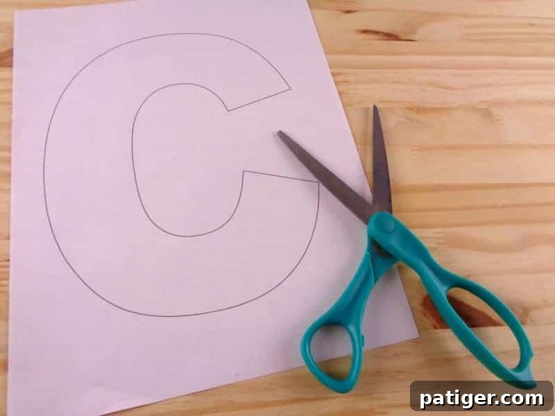 Child-safe scissors cutting out the printable letter C template from paper, preparing for the craft.