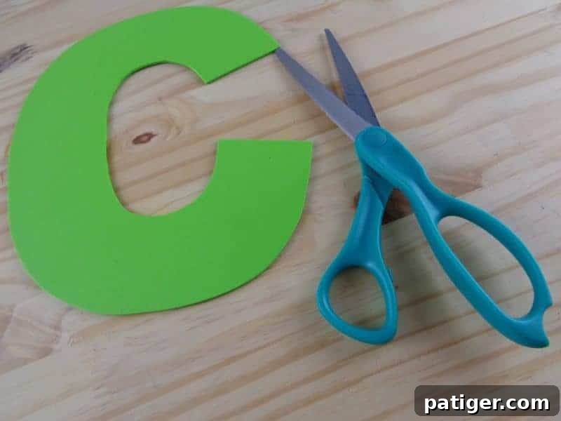 A child's hand precisely cutting the traced letter C shape from craft foam, developing fine motor skills.
