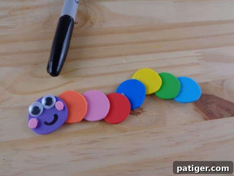 Seven colorful craft foam circles are carefully glued together in a row, forming the segmented body of the caterpillar.