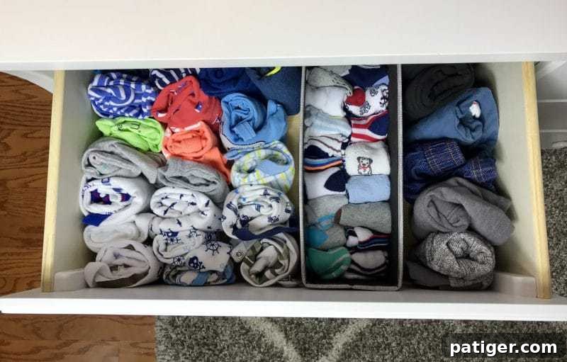 Baby clothing, socks, and onesies folded neatly in a drawer with dividers. 